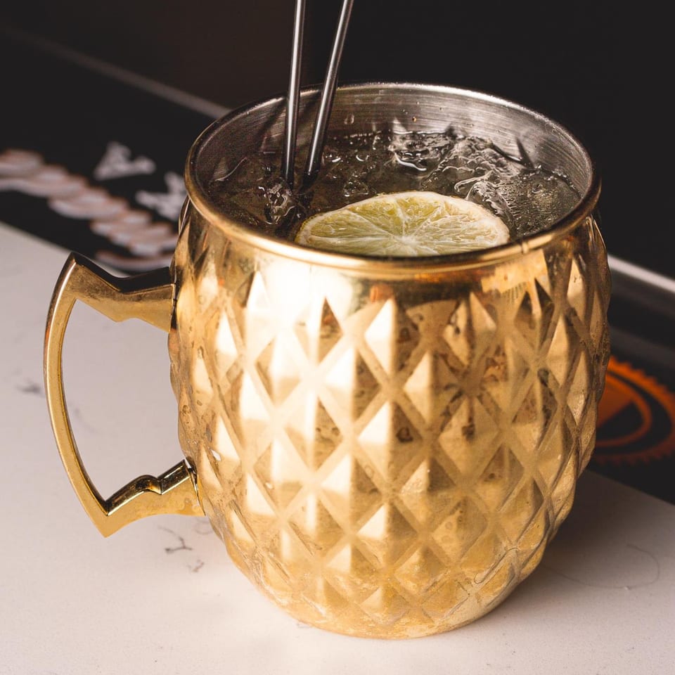A golden Moscow Mule mug filled with ice, a lime slice, and two metal straws.
