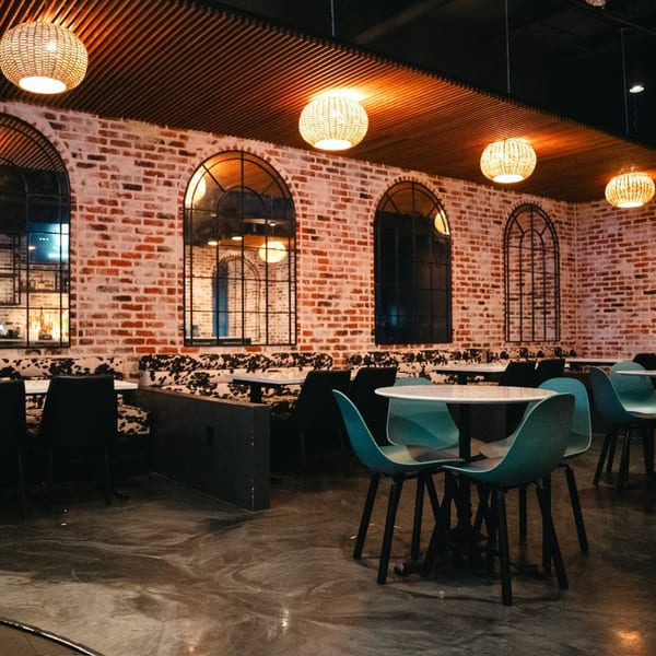 PizzaMe! dining room with brick walls, arched windows, woven pendant lights, and modern tables.