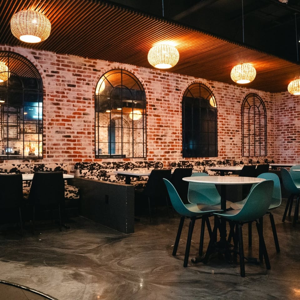 Interior of PizzaMe! restaurant with brick walls, arched windows, woven light fixtures, and modern seating.