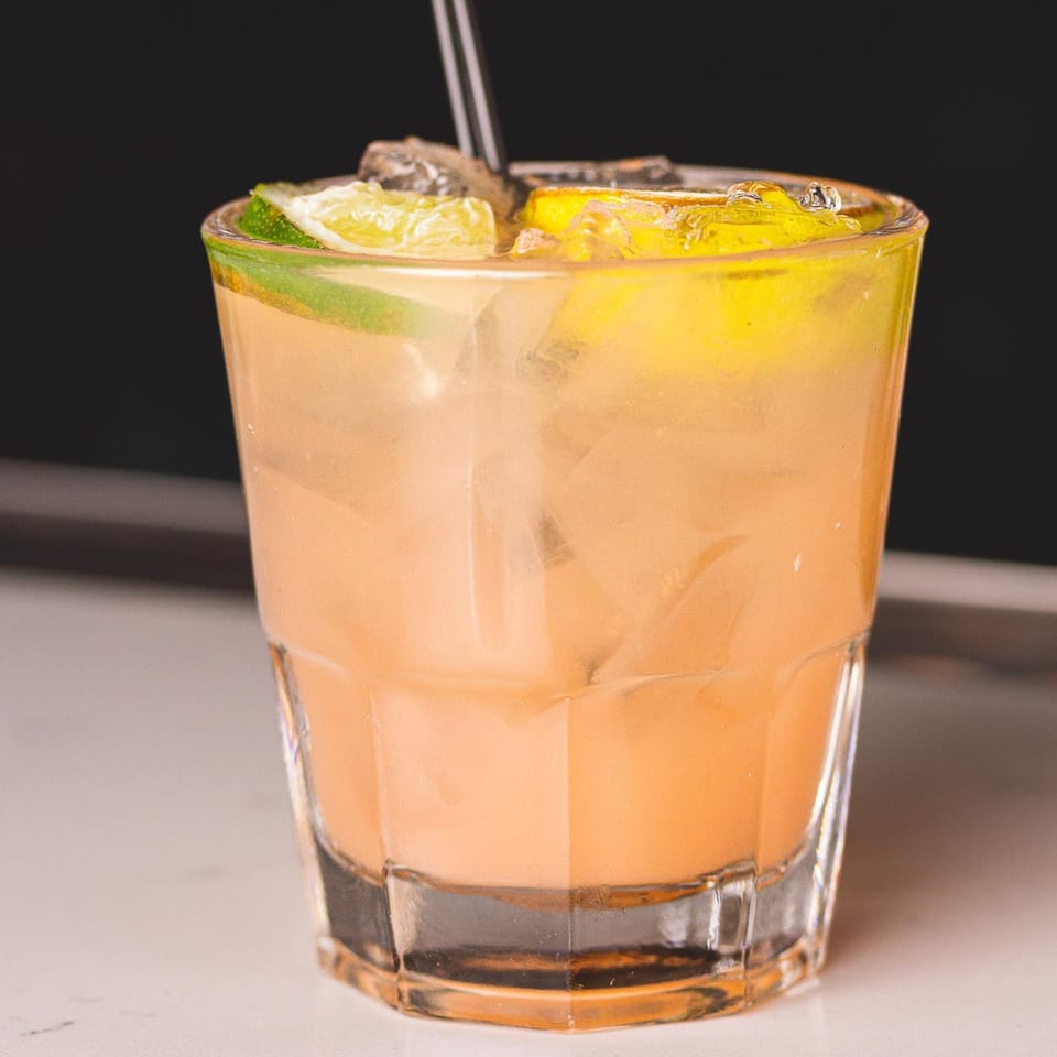 A refreshing orange cocktail with ice, lime, and lemon slices, served in a clear glass.