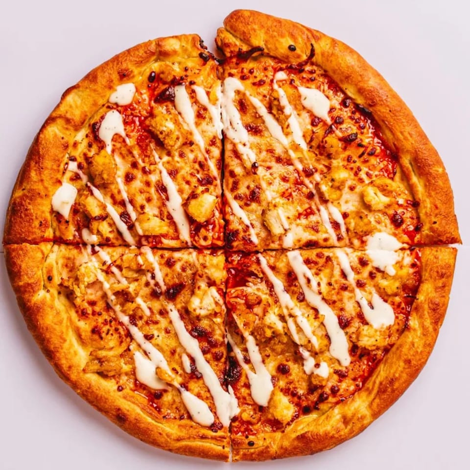 A whole PizzaMe! pizza, cut into four slices, topped with chicken and white sauce.
