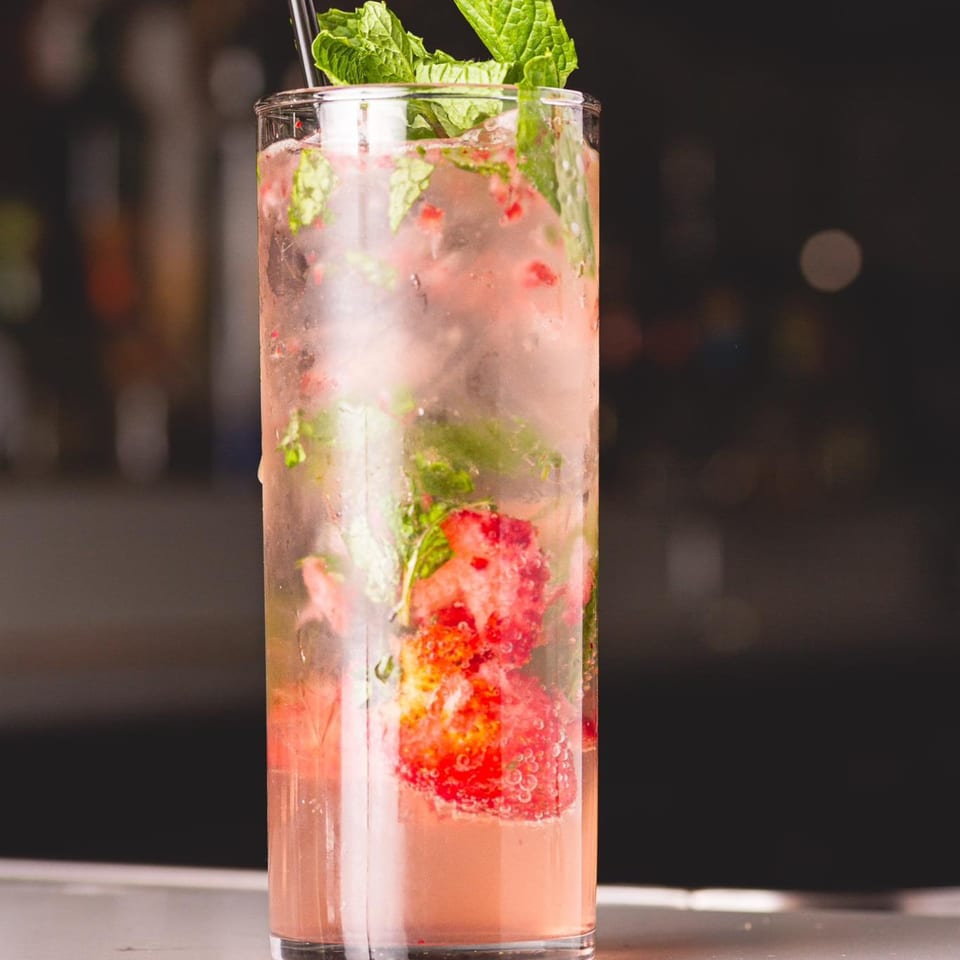 Refreshing strawberry mojito with mint leaves and ice in a tall glass, against a dark background.
