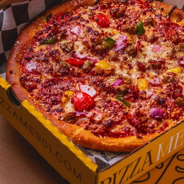 A close-up of a PizzaMe! pizza with red sauce, cheese, and colorful toppings in a yellow box.