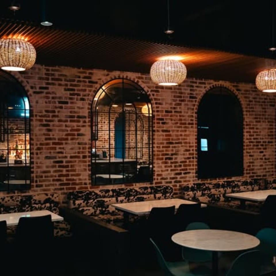 PizzaMe! restaurant interior with brick walls, arched mirrors, woven pendant lights, and booth seating.